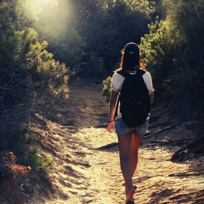 rear-view-woman-hiker-dirt-road-forest